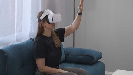female-user-is-using-HMD-display-for-viewing-interior-of-modern-flat-sitting-on-couch-in-living-room-modern-technology-of-virtual-reality